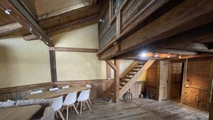 A rustic wooden interior with a dining area, a staircase, and a large wooden door. - Central 3-BR Apartment for 6 with WiFi, Parking & Spa Access (Les Carroz d'Arâches)