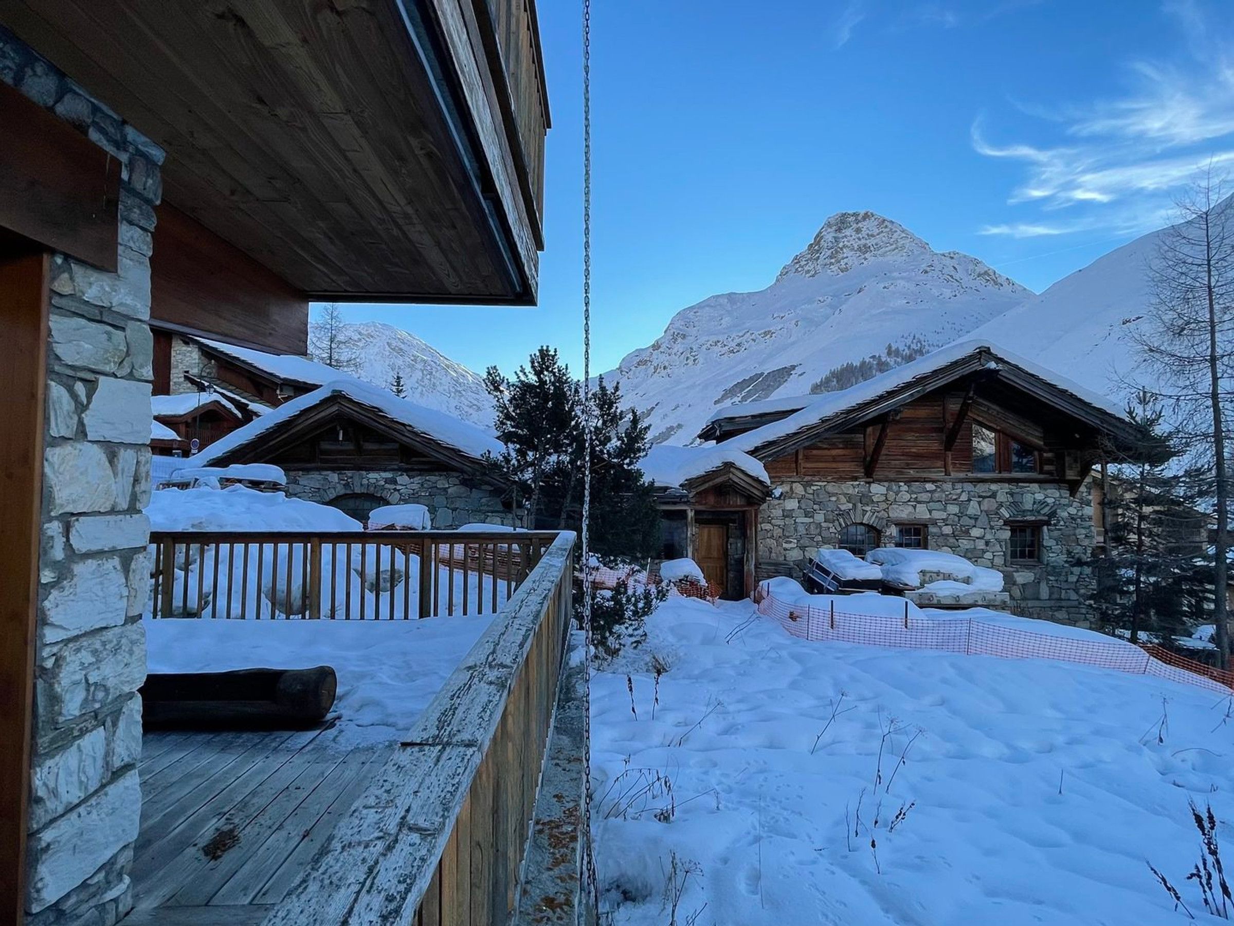A snow-covered mountain lodge with stone walls and wooden beams, featuring a wooden deck and a view of the surrounding snowy landscape.