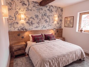 A bedroom with a wooden headboard, a bed with multiple pillows, bedside tables, wall-mounted lamps, and a window with a view. - Rustic Apartment with Fireplace, Garage, and WiFi in Val-d'Isère (Val-d'Isère)