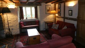 A cozy living room with a stone wall, wooden beams, a red sofa, a bench, and a lamp. - Luxurious Cottage with Lovely Views in Rural Location (Norton Presteigne)