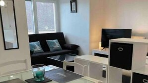 A compact living space with a dining area, a sofa, a television, and storage units.
