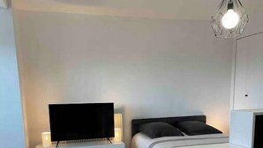 A modern, minimalistic bedroom with a bed, a TV, a desk, and a hanging light fixture.
