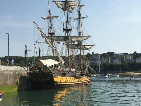 Een groot zeilschip afgemeerd in een haven, met gebouwen op de achtergrond.