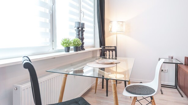 A modern dining area with a glass table, two chairs, a lamp, and a window with blinds. - Central, modern designer appartment in downtown Stuttgart (Stuttgart)
