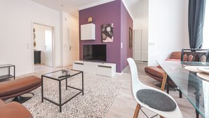 A modern living room with a flat-screen TV, a glass dining table, and a purple accent wall. - Central, modern designer appartment in downtown Stuttgart (Stuttgart)