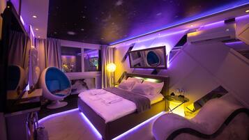 Een moderne slaapkamer met een sterrenhemel, een bed met netjes gevouwen handdoeken, een unieke blauwe stoel en een comfortabele bank.