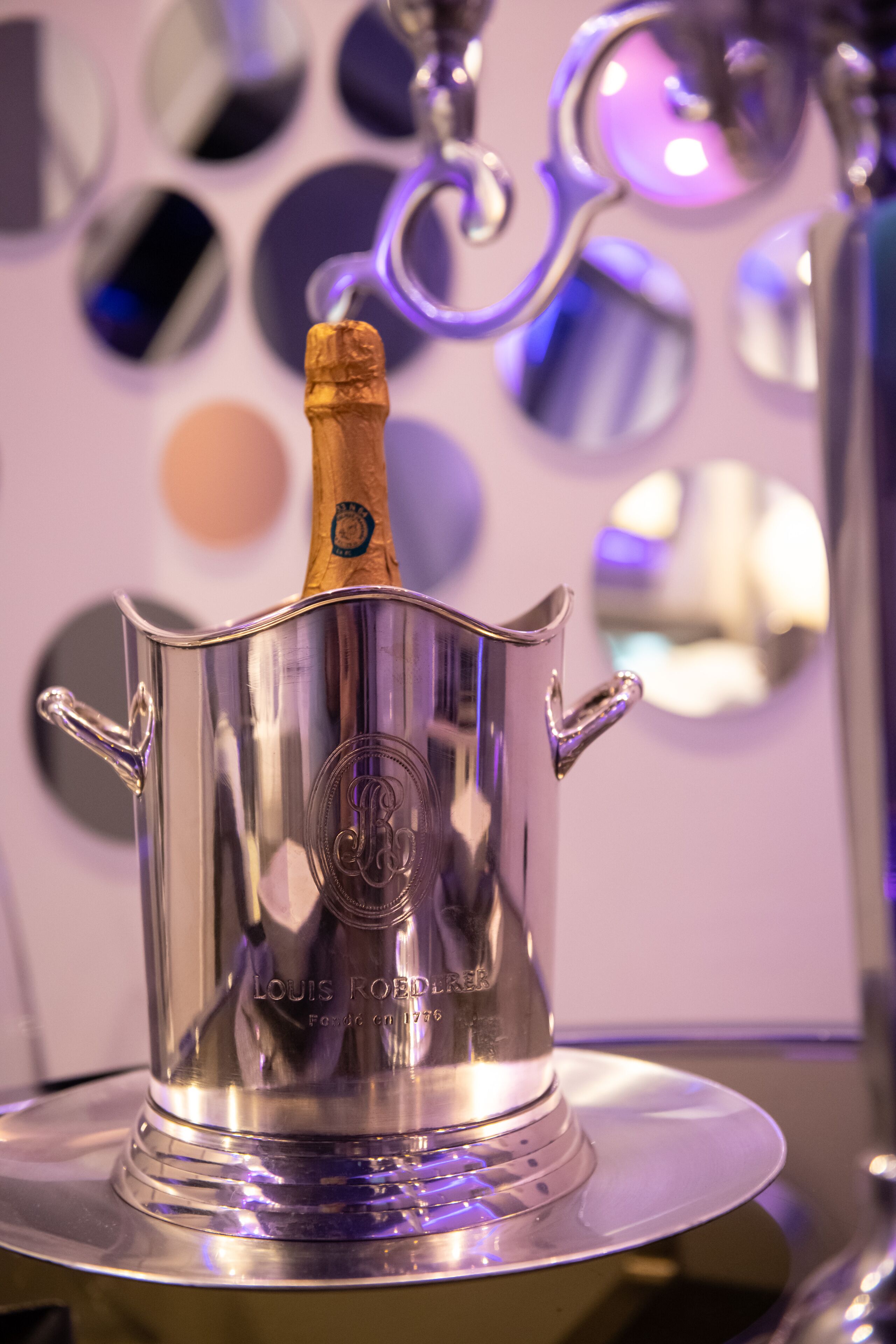 A silver champagne bucket with a cork, placed on a reflective surface.