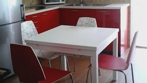 Una cocina compacta con una mesa blanca y sillas rojas, un microondas y un refrigerador.