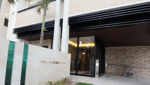 A modern building entrance with a stone facade, a glass door, and a small garden area.