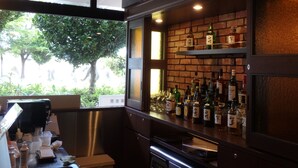 A bar area with a brick wall, shelves with liquor bottles, and a view of greenery outside.