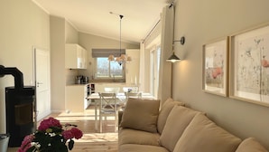 Una sala de estar acogedora con un sofá color beige, un comedor con mesa y sillas, una cocina con armarios blancos y una chimenea.