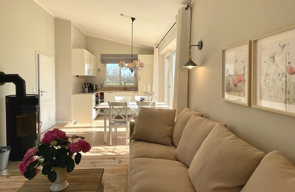 A cozy living room with a beige sofa, a dining area with a table and chairs, a kitchen with white cabinets, and a fireplace.