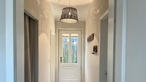 Un pasillo con piso estampado, una puerta blanca con paneles de vidrio y una lámpara colgante.