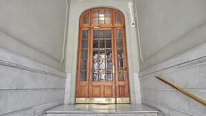 Una imponente puerta de madera con paneles de vidrio que da a una escalera de mármol con barandilla de latón.