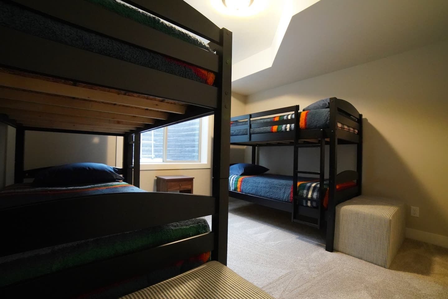 A dormitory room with bunk beds, a small wooden nightstand, and a window providing natural light.