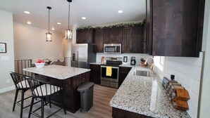 A modern kitchen with dark wood cabinets, granite countertops, stainless steel appliances, and pendant lighting. - Luxurious Family Home in Driggs - Hot Tub (Driggs)