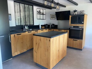 Eine moderne Küche mit Holzausbau, einer schwarzen Arbeitsplatte, einem eingebauten Backofen, einer Mikrowelle und einer großen Kochinsel.