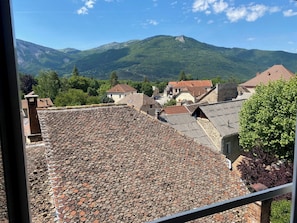 Blick auf eine Stadt mit terrakottafarbenen Dächern, Steinbauten und einer gebirgigen Kulisse.