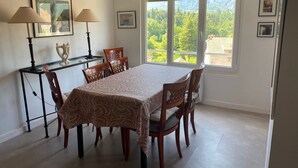 Un comedor con una mesa y sillas, una lámpara, una mesita con un adorno y una ventana con vistas a zonas verdes.