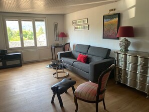Ein Wohnzimmer mit grauem Sofa, einem karierten Sessel, einem kleinen Tisch, einem Schrank und einem Bild an der Wand.