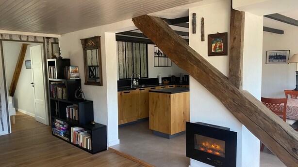 Un interior moderno con una escalera de madera, una chimenea, una zona de cocina y una estantería.