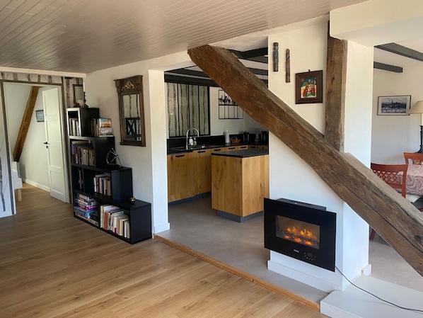 A modern interior with a wooden staircase, a fireplace, a kitchen area, and a bookshelf. - Apartment in the mountains, 30 minutes from ski resorts (LA ROCHE DES ARNAUDS)