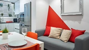 A modern living room with a grey sofa, red cushions, and a white dining table.