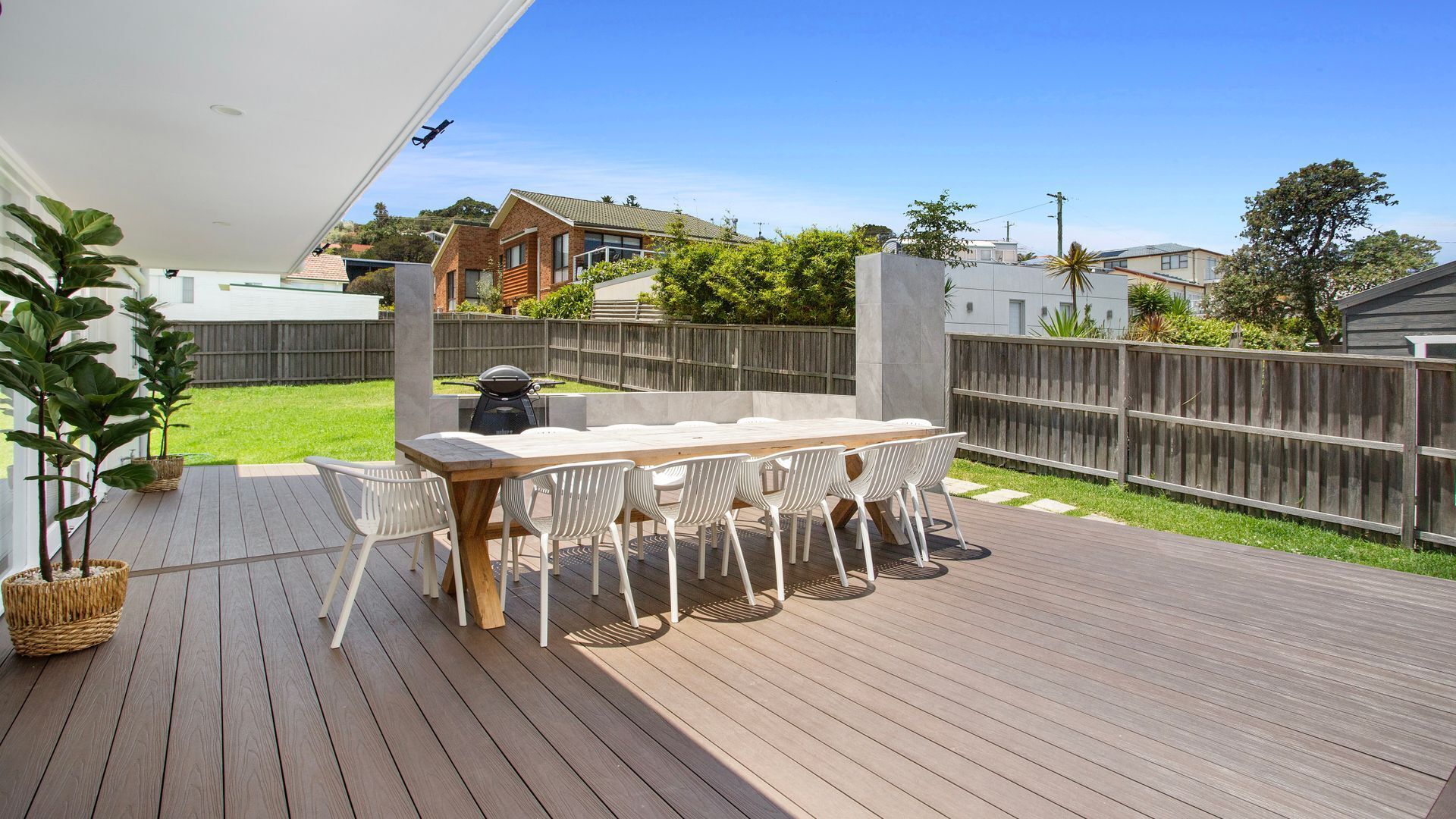 Une terrasse en bois avec une table et des chaises, entourée d’une clôture en bois et de verdure.