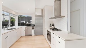 A modern kitchen with white cabinetry, stainless steel appliances, and a large window providing a view of the outside. - Prime Position -  Family Getaway (Gerroa)