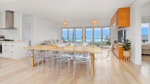 A modern kitchen with a large island, clear chairs, and a view of the ocean. - Prime Position -  Family Getaway (Gerroa)