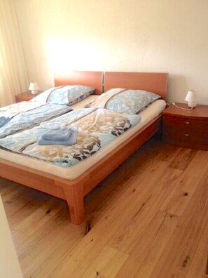 Un lit simple avec une tête de lit en bois, une table de chevet avec une lampe et un plancher en bois.