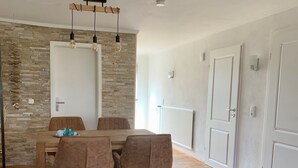 Un coin repas avec une table en bois et deux chaises rembourrées, un mur en pierre et un luminaire au plafond.