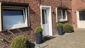 Un bâtiment en briques avec deux fenêtres, une porte et deux plantes en pot.