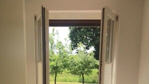Une porte ouverte donnant sur une terrasse en briques, avec une pelouse et des arbres.
