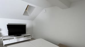Un dormitorio con una cama, televisión y un ventanal pequeño.
