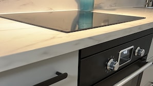 Una cocina de diseño moderno, con un horno negro con reloj digital, un lavamanos de acero inoxidable y armarios blancos.