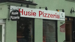 Un edificio de dos pisos con fachada verde y un letrero que dice Husie Pizzeria.