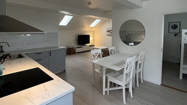 Una cocina moderna con estufa integrada, armarios blancos y una zona de comedor con mesa y sillas.