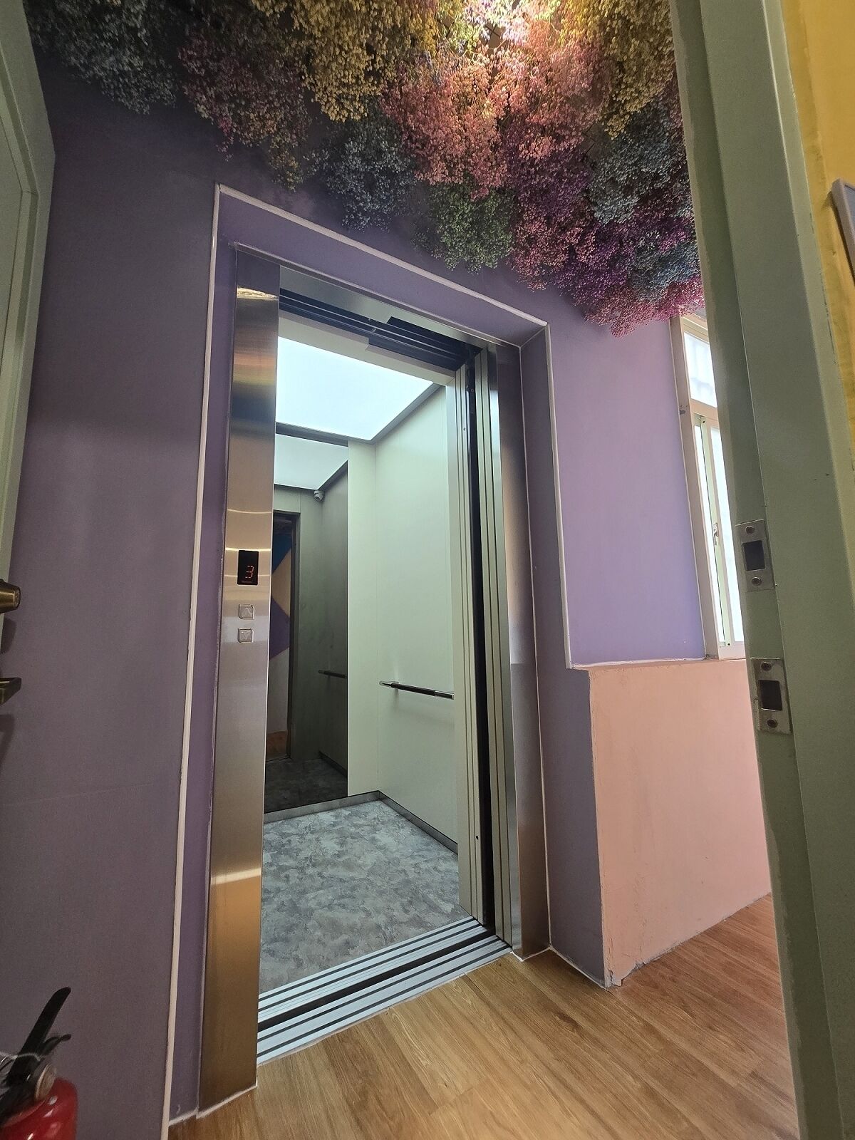 An interior view of a hallway with a metallic elevator door, a wooden floor, and a ceiling with a decorative tree design.