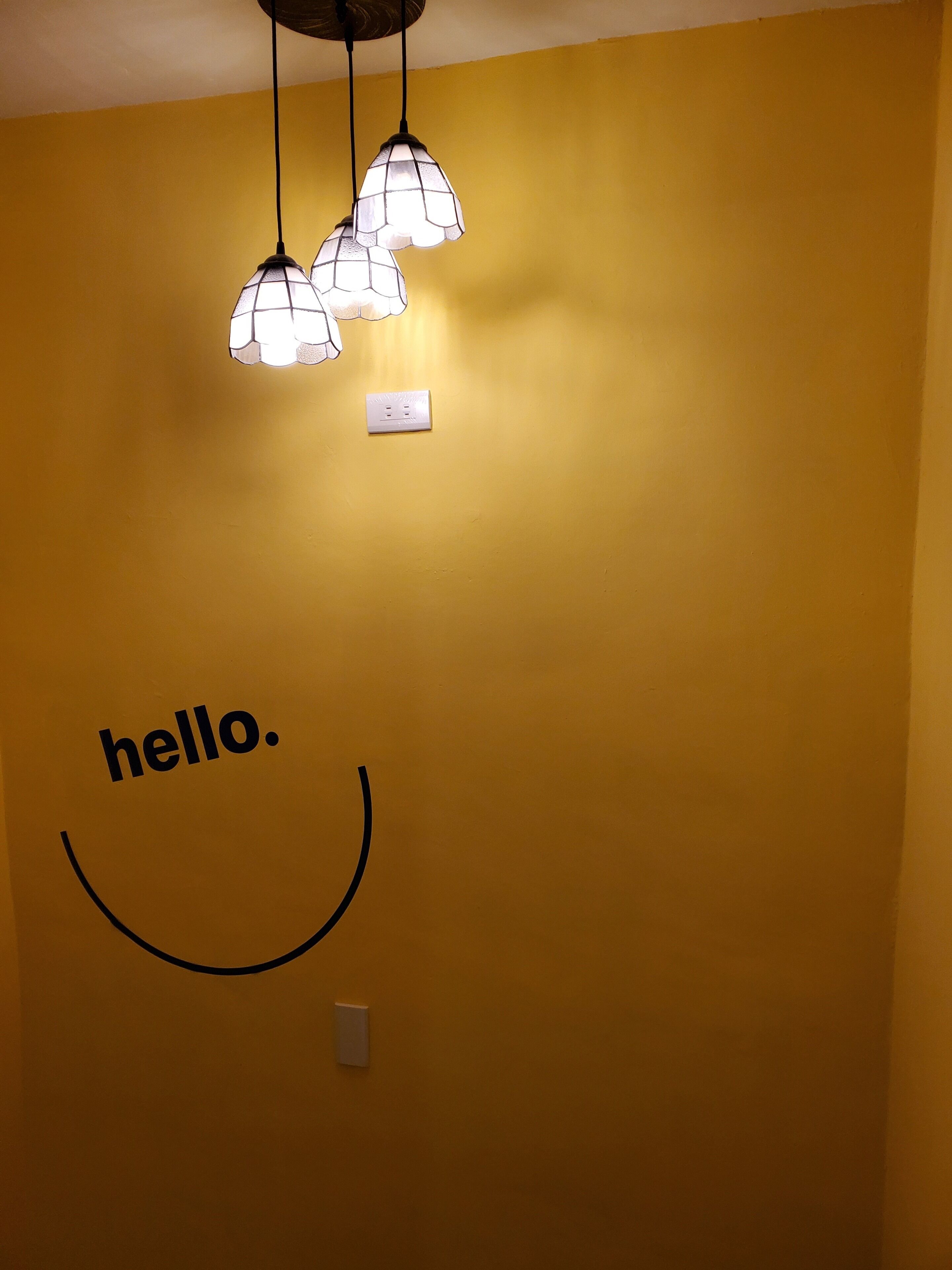 A yellow wall with a 'hello.' sign and a light fixture.