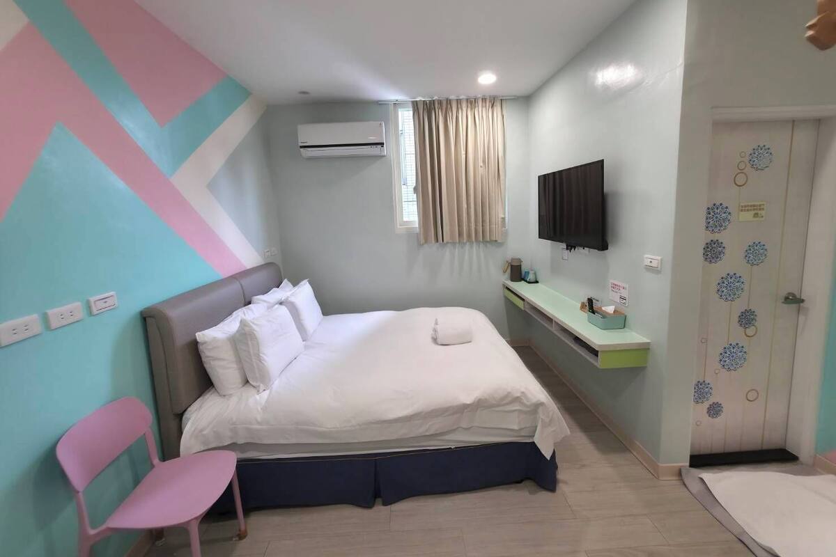 A bedroom with a bed, a desk, a chair, an air conditioner, a TV, and a door with decorative elements.