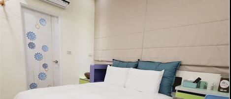 A hotel room with a bed, a desk with a chair, a window, and an air conditioning unit.