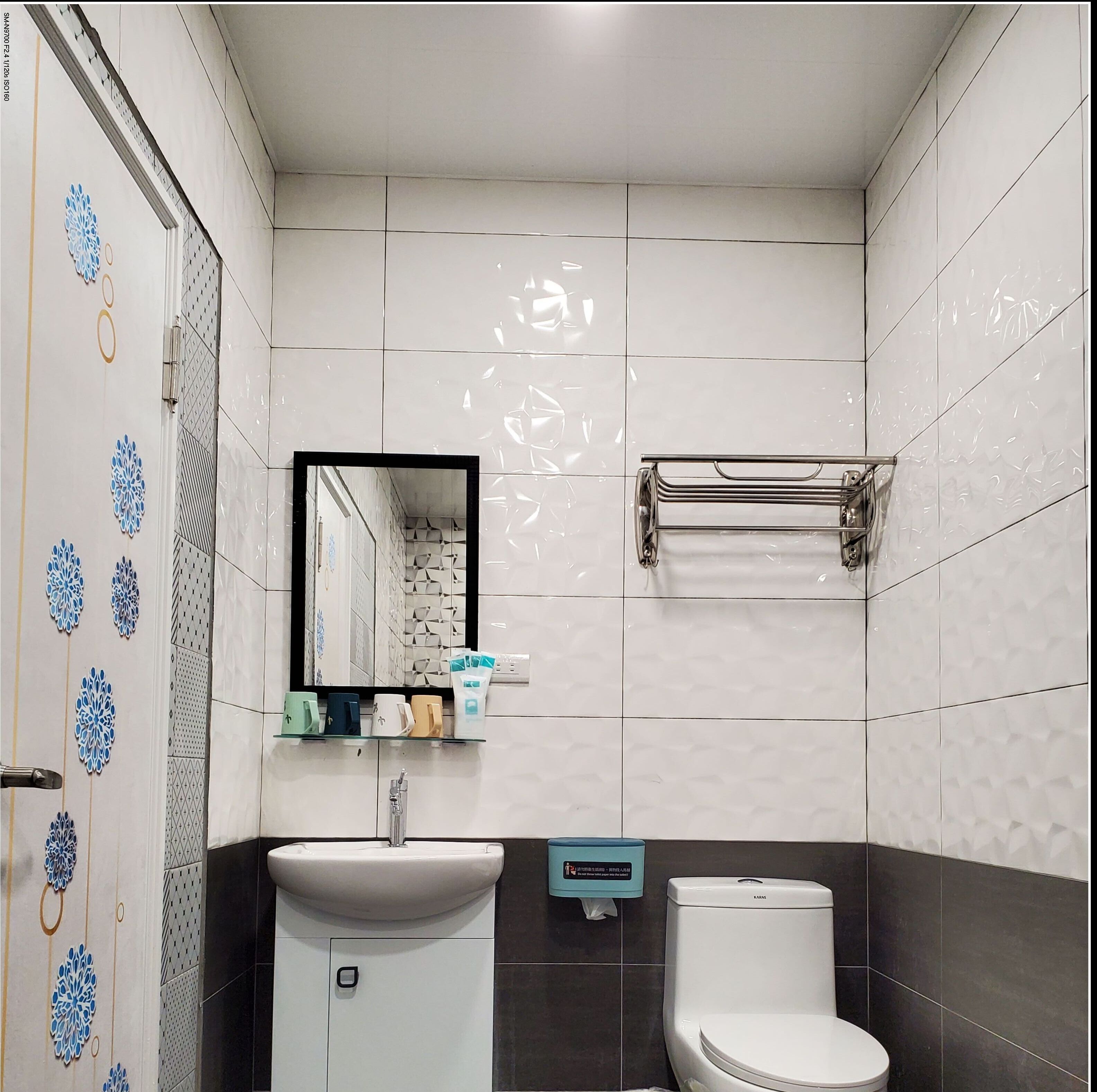 A bathroom with a white sink, a toilet, and a mirror. There are decorative tiles on the walls and a towel rack above the toilet.