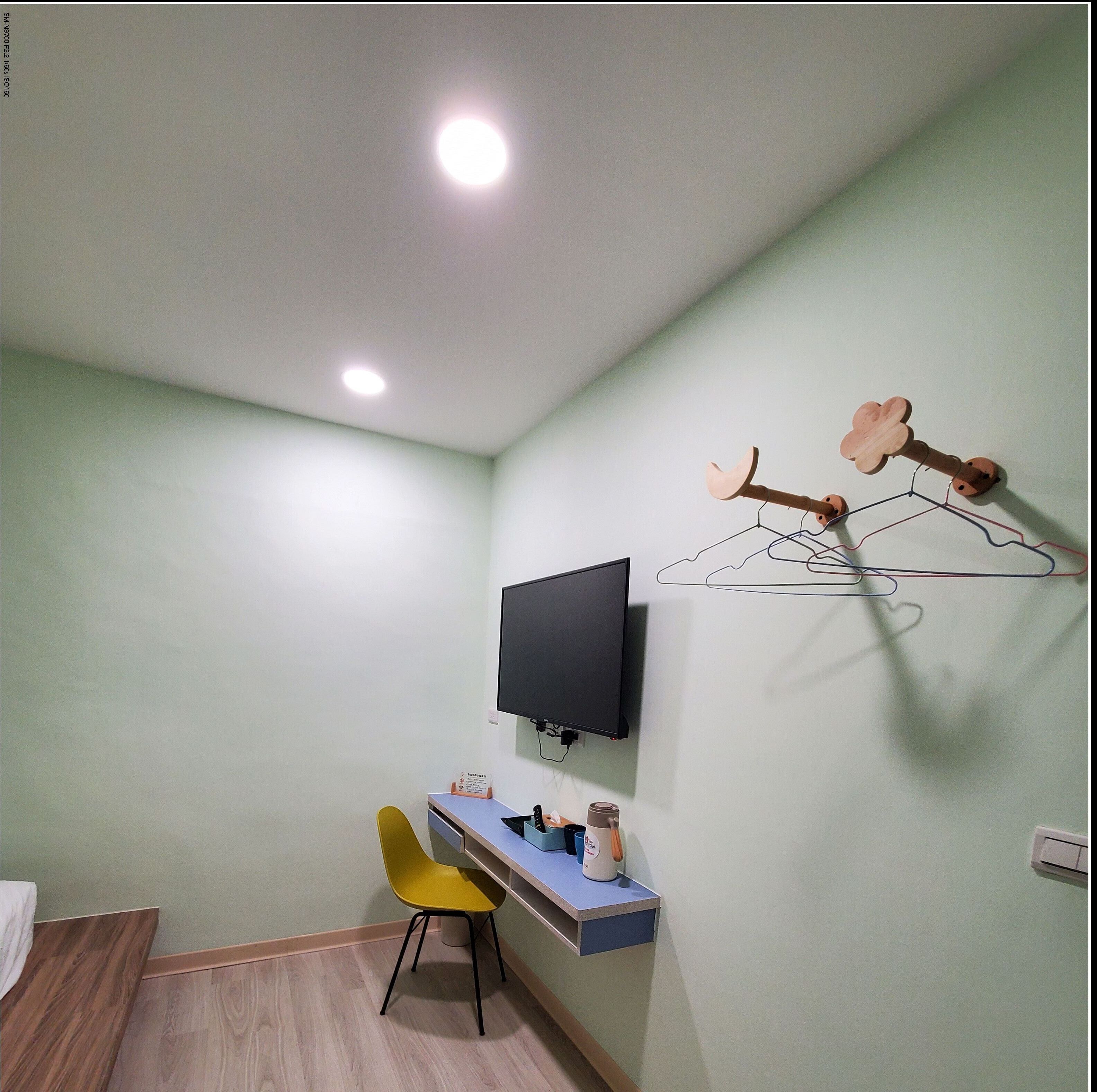 A room with a desk, a chair, a television mounted on the wall, and a decorative wall art piece.