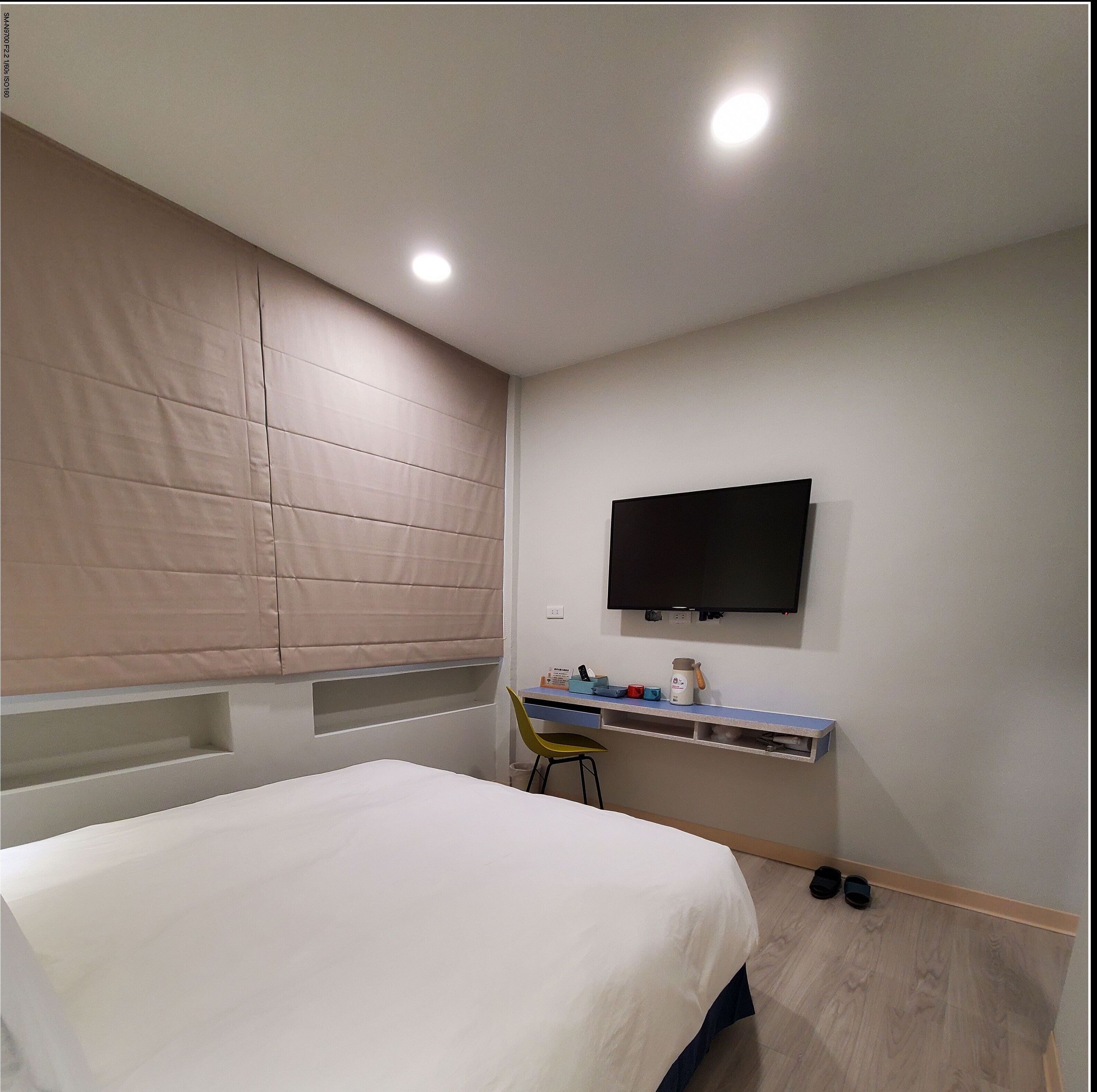 Un dormitorio con una cama, un escritorio con silla, un televisor y una ventana con persianas.