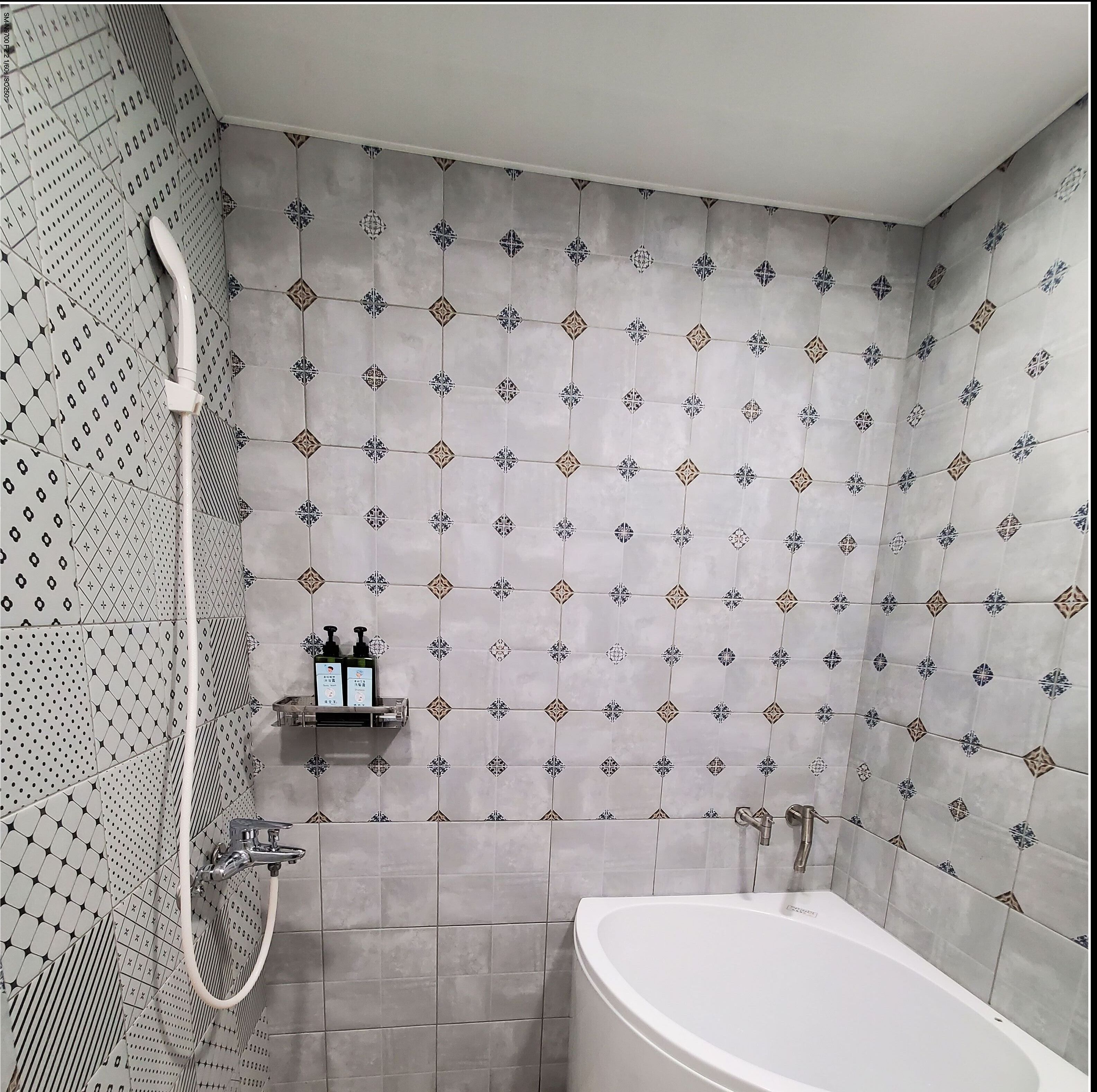 Une salle de bain avec une baignoire blanche, une douche avec un pommeau flexible et une étagère murale contenant des articles de toilette.