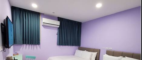 A hotel room with two beds, a desk with a chair, an air conditioner, and a TV mounted on the wall.
