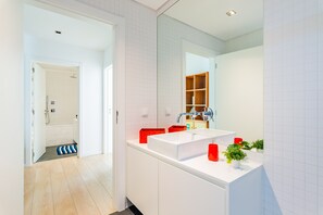 A modern bathroom with a white sink, mirror, and tiled walls. There is a shower area visible in the background.