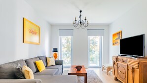 A modern living room with a grey sofa, wooden coffee table, and a TV on a wooden cabinet. - Santo Amaro Beach Apartment (Oeiras)