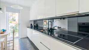 A modern kitchen with white cabinets, a black countertop, and stainless steel appliances. - Santo Amaro Beach Apartment (Oeiras)